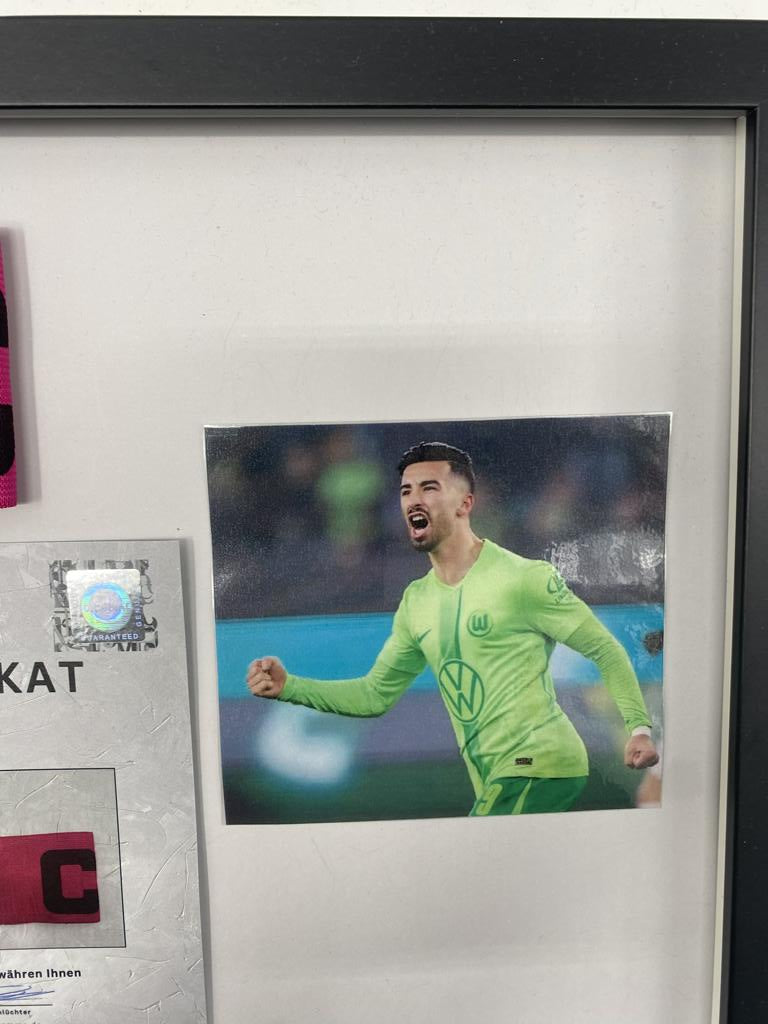 Brazalete de capitán firmado por Mohamed Amoura en un marco de Wolfsburg, certificado de autenticidad.
