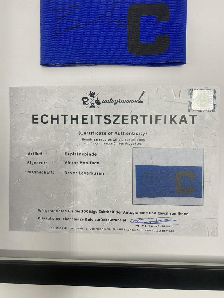 Captain's armband signed by Victor Boniface in a Bayer Leverkusen frame. Autograph