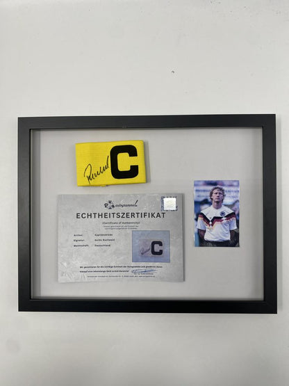 Captain's armband signed by Guido Buchwald in a Germany Football autograph frame